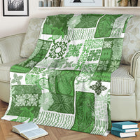 Green patchwork quilt blanket with tiki and leaf patterns, spread over a couch.
