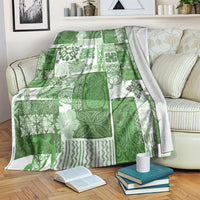Green and white tiki-inspired quilt blanket with geometric patchwork, folded on a couch.
