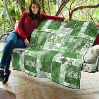 Green and white tiki patchwork quilt with tropical floral motifs and black trim draped outdoors