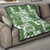 Green and white tiki patchwork quilt with tropical floral motifs and black-trim edge on sofa
