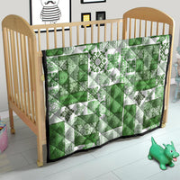 Green and white tiki patchwork quilt with tropical floral motifs and black trim on baby bed