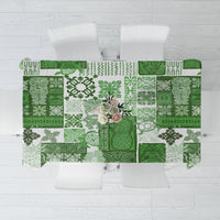 Green patchwork tiki tablecloth with repeating motifs, laid flat with visible panels