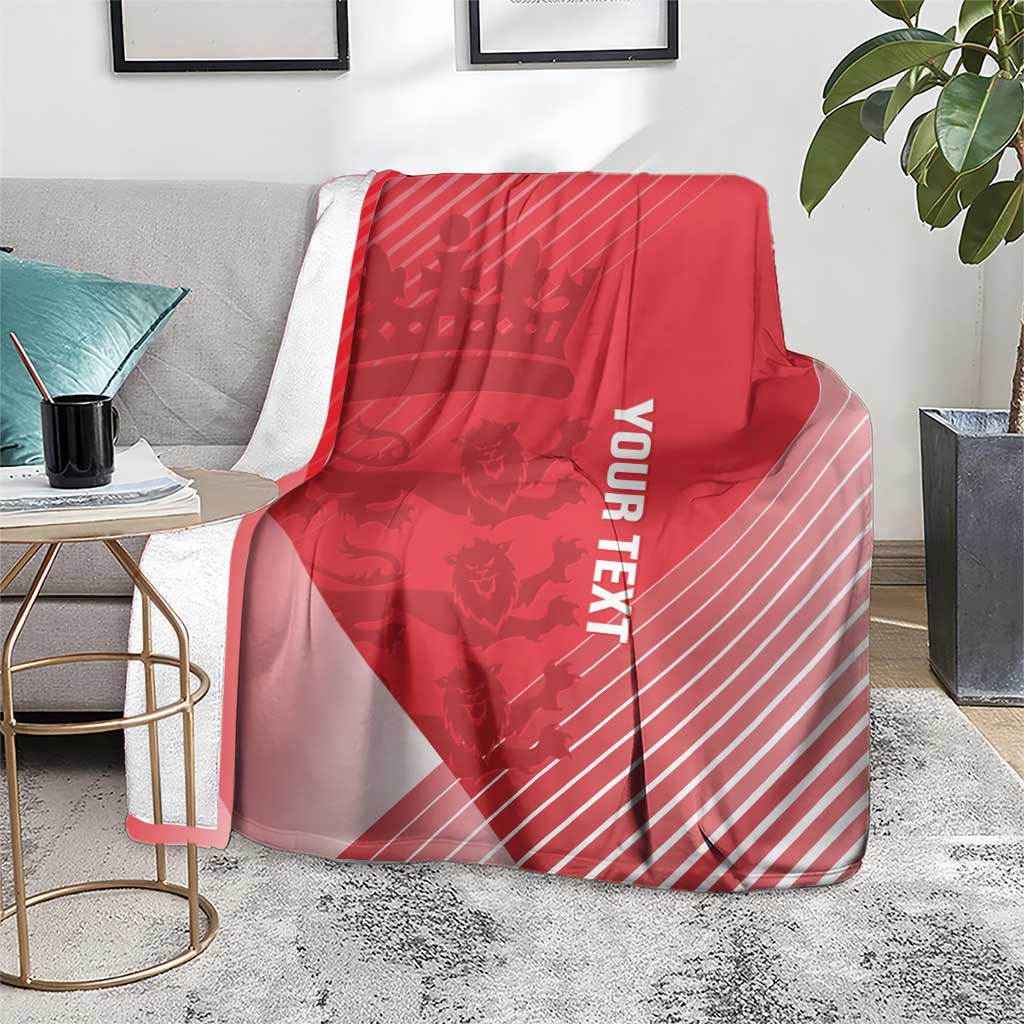 Red cricket blanket over gray sofa with crown motif, diagonal stripes, and vertical 'YOUR TEXT'