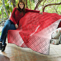 Red and white diagonal quilt blanket with diamond quilting and black trim, laid on sofa