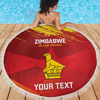 Red round beach blanket with white fringe, Zimbabwe text and central yellow bird design.