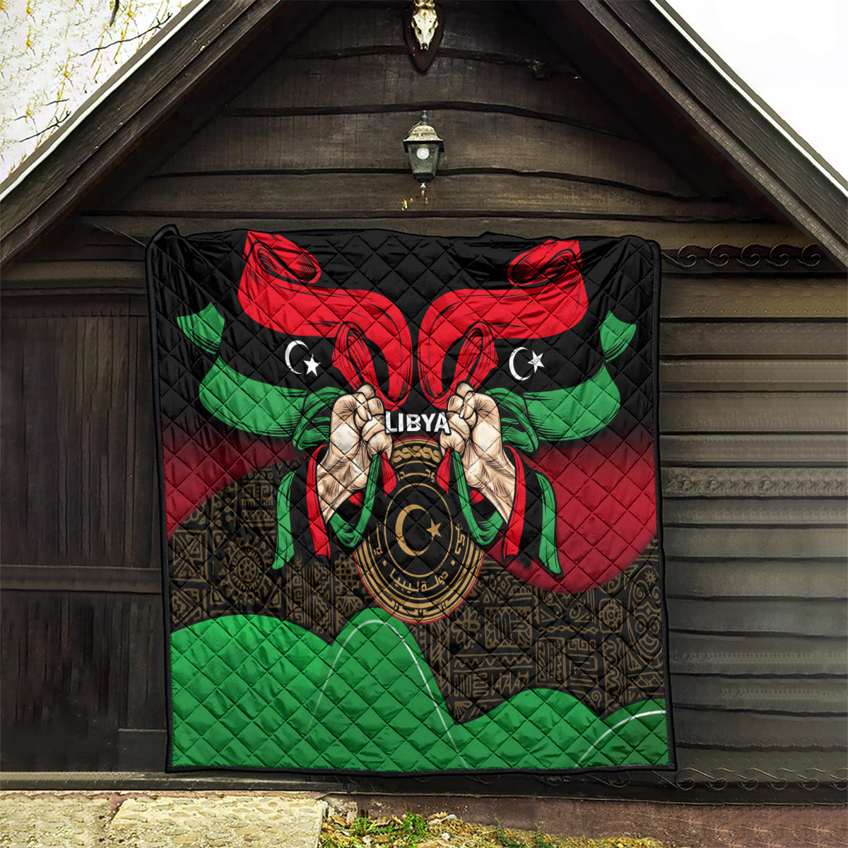 Libya flag-style quilt hanging outdoors with red, black, green eagle-like design.