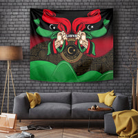 Wall tapestry with black base, red-and-green ribbons, central Libya emblem held by hands.
