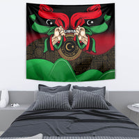 Wall tapestry with black background, red ribbons and green accents, Libya emblem with hands.