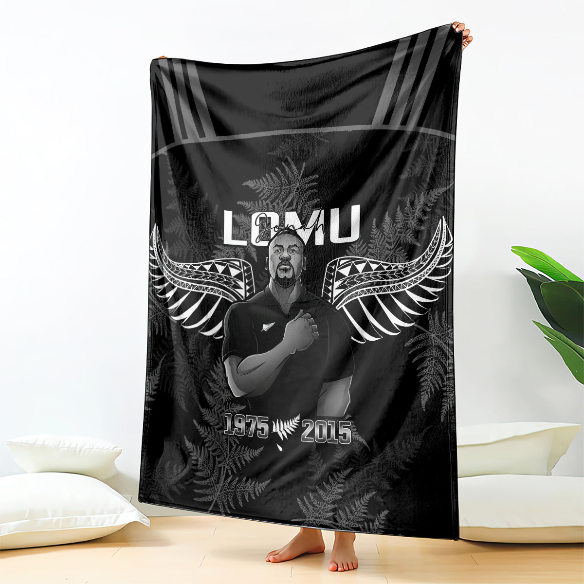 Black rugby blanket with winged fern pattern and portrait graphic, draped on bed