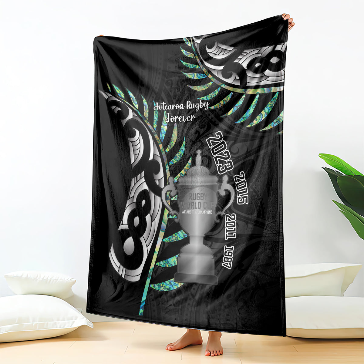 Black rugby blanket with fern and trophy-themed graphics, draped over an open edge