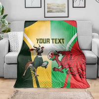 Rugby blanket on gray couch with green, red, and yellow flag design, dragon and goat mascots