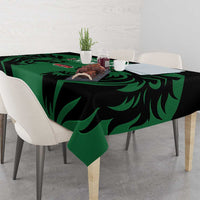 Green and black leaf-pattern tablecloth on dining table with plates and a vase