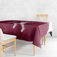 Maroon tablecloth with white Qatar cricket graphics and serrated edge, on wooden table.