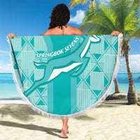 Fringed round teal blanket with “YOUR TEXT” and Springbok Sevens logo, held stretched on sand.