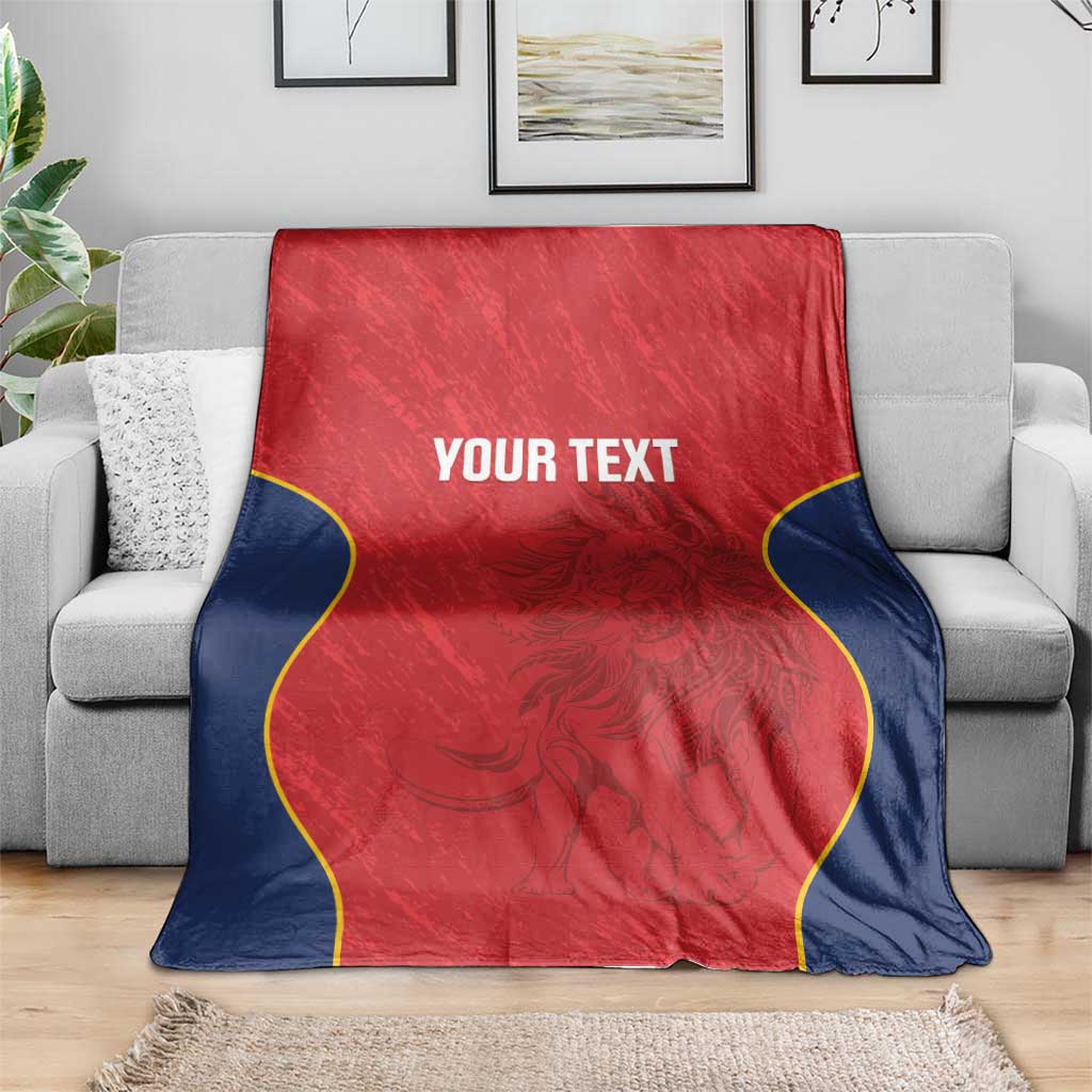 Red Spain rugby blanket on gray sofa, navy sides with yellow piping and “YOUR TEXT”.