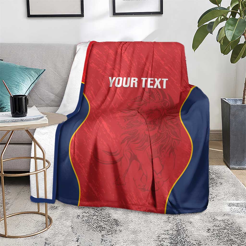 Red Spain rugby blanket on floor beside a table, navy edges with yellow trim and “YOUR TEXT”.