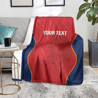 Red Spain rugby blanket on floor beside a table, navy edges with yellow trim and “YOUR TEXT”.