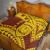 Gold and maroon quilt covering a bed, with geometric design and central shield crest