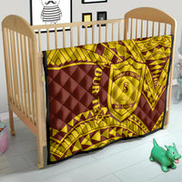 Gold and maroon quilt laid over a crib, geometric pattern and central shield crest