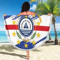 Person holding a round Cabo Verde beach blanket with crest, blue white red star pattern, fringe
