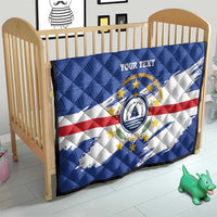 Quilted blanket on baby crib with blue flag pattern, white/red stripes, crest, 'YOUR TEXT'.