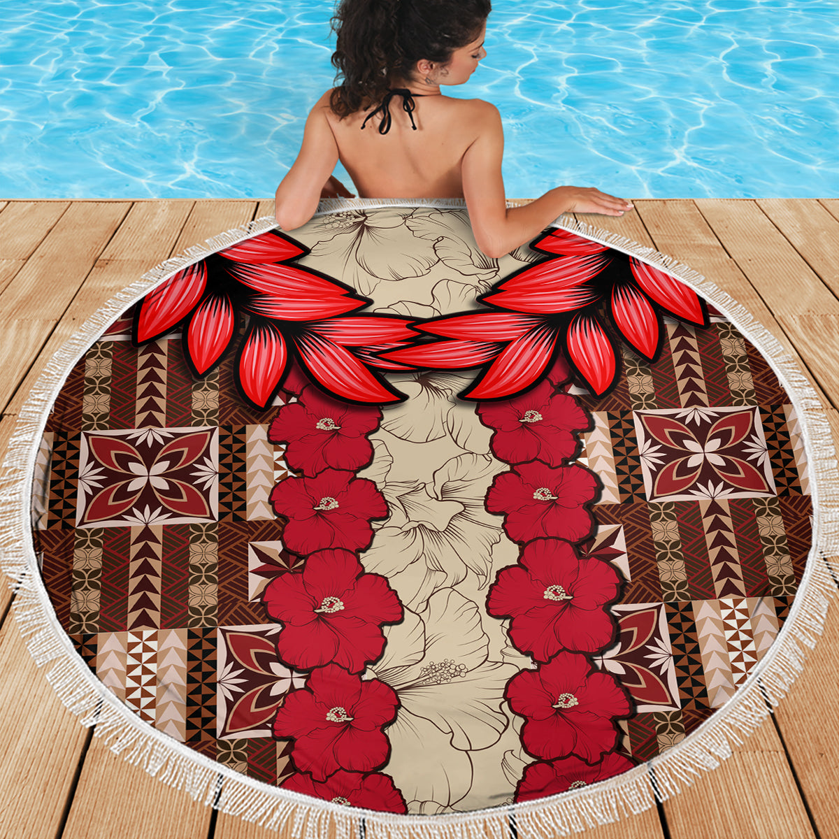 Round beach blanket showing red hibiscus tapa-style motif, central floral garland, fringe border