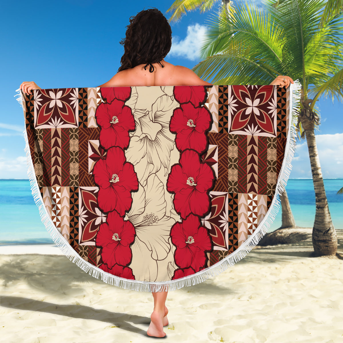 Round beach blanket spread out with red hibiscus tapa pattern, central floral garland, fringe
