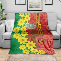 Red and green Ethiopian throw blanket on a gray couch with yellow flowers and gold cross