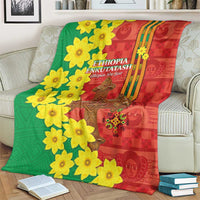 Red and green Ethiopian blanket laid on a bed with yellow blossoms and gold cross center