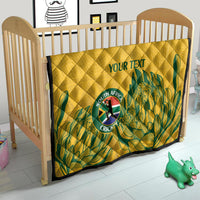 Yellow quilt on crib with diamond quilting, green leaf pattern, and “YOUR TEXT” center.