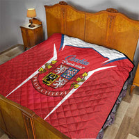 Red Czechia crest quilt laid on bed with white-blue chevron and diamond quilting