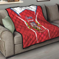 Red Czechia crest quilt draped on sofa, showing white-blue chevron and diamond stitching
