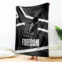 Black throw blanket with Mandela portrait and white stripes, spread on floor beside pillows