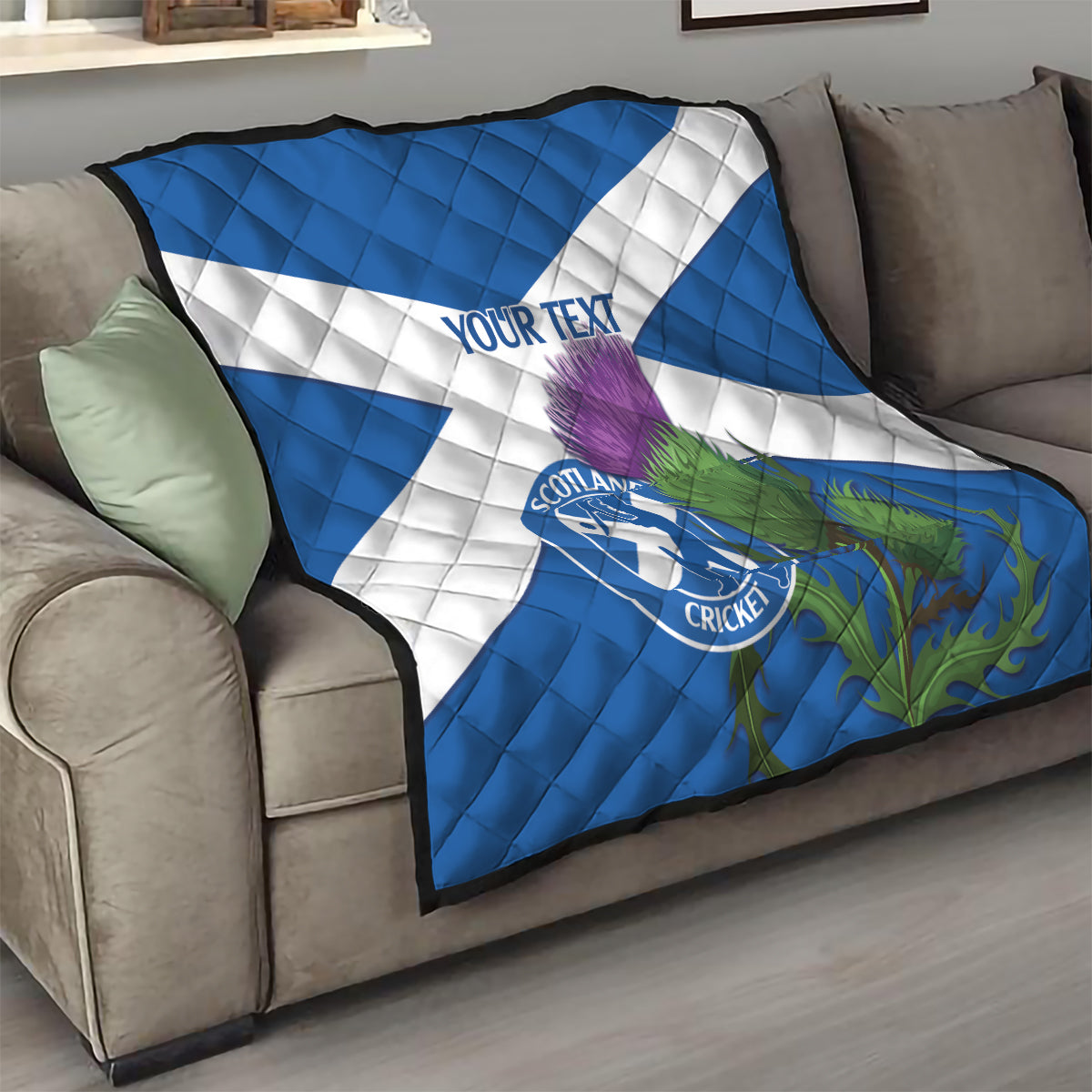 Blue and white quilt draped on sofa with Scotland Cricket emblem, thistle artwork, 'YOUR TEXT'.