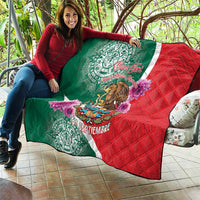 Green and red quilt with eagle and purple flowers held outdoors on patio seating.