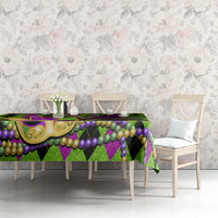 Colorful Mardi Gras tablecloth on table with jester mask, green and purple bead garlands and scallop trim