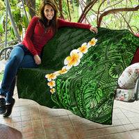 Green quilted blanket spread out, showing green tropical leaf artwork with yellow-white plumeria flowers.