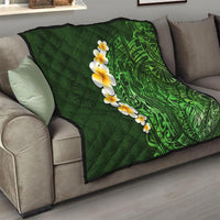 Green quilted throw blanket on a sofa, with green Polynesian leaf pattern and yellow plumeria blooms.