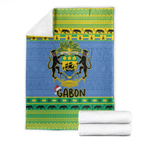 Folded blue Christmas blanket with coat of arms crest, green-yellow border, beside white towels