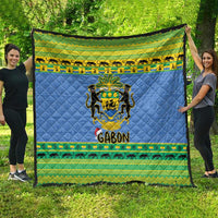 Blue quilt blanket draped outdoors with Gabon coat of arms and green animal stripe border.