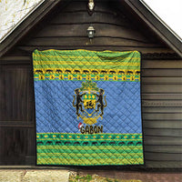 Blue quilt blanket hanging on wooden wall with Gabon coat of arms and green trim.