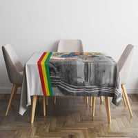 Rectangular Christmas tablecloth with gray church scene, multicolor stripe trim, and chairs
