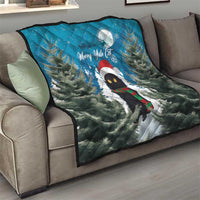 Blue quilt blanket draped on a sofa with cat in Santa hat, pine trees, and moon.