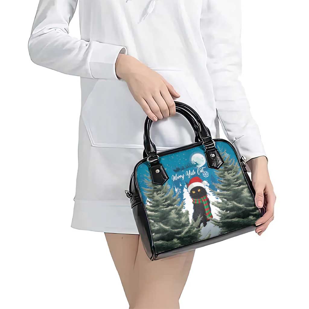 Blue shoulder handbag with black handles and festive cat in pine tree scene, worn.