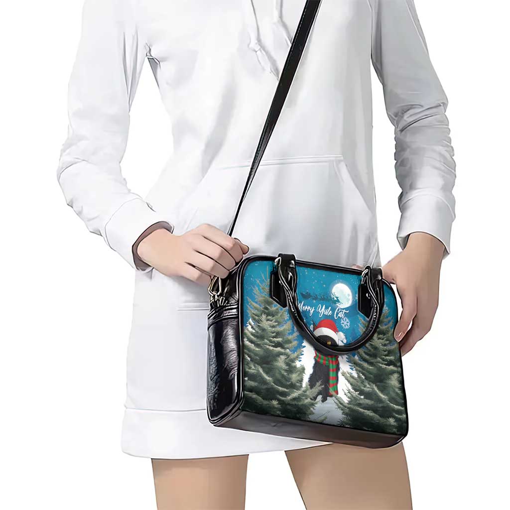 Blue crossbody handbag with black strap and Merry Yule cat print, worn over dress.