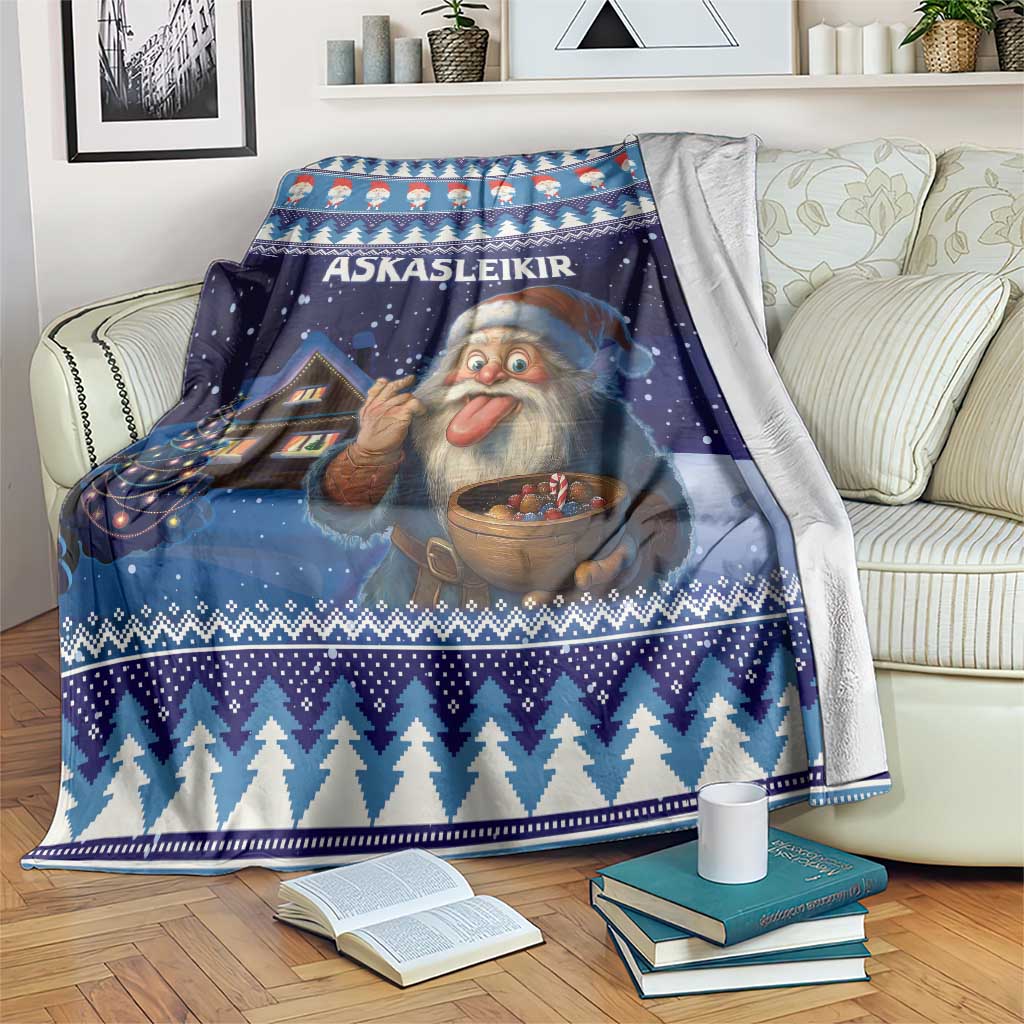 Blue holiday blanket over couch with Yule lad face, bowl, house, and zigzag trees