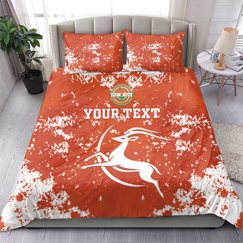 Orange graphic duvet and two pillows with white splatter, circular emblem and 'YOURTEXT' text