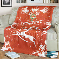 Orange football blanket with white splatter print, crest emblem and “YOUR TEXT”