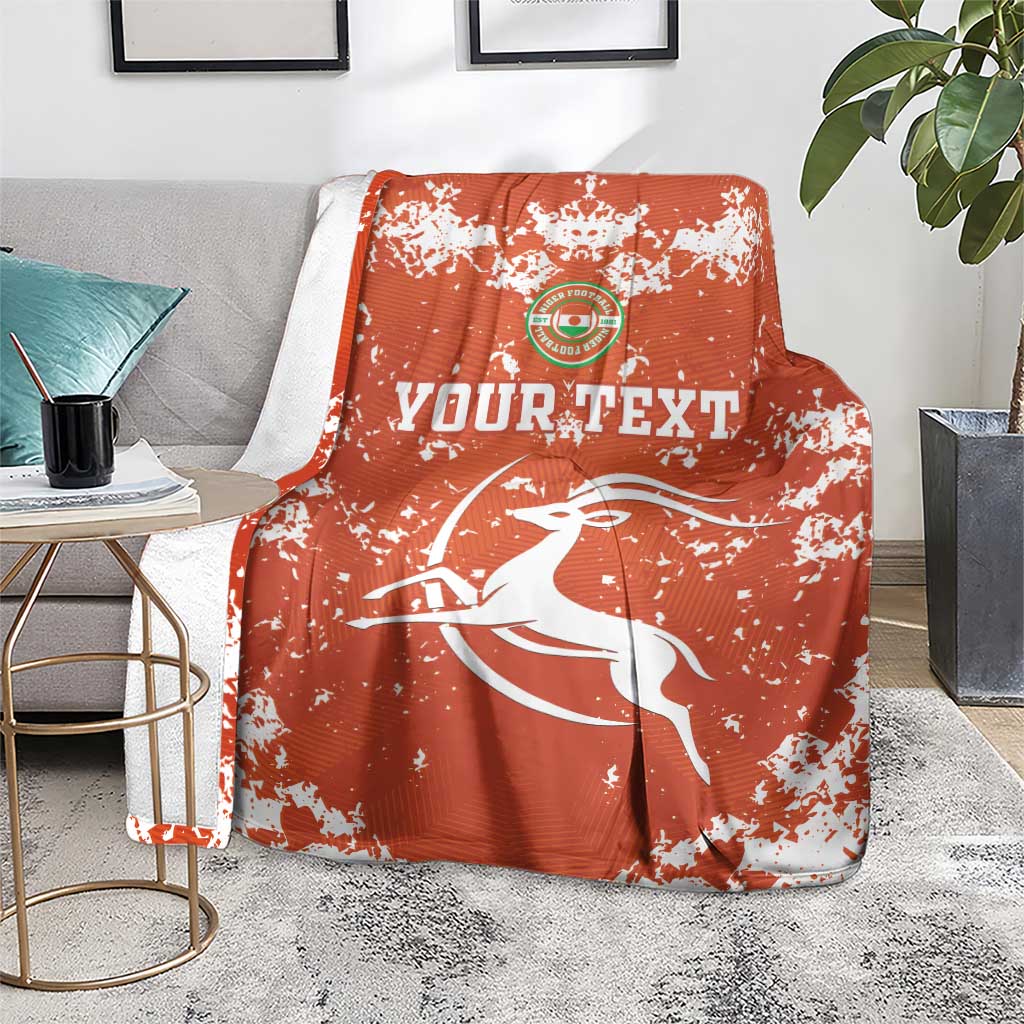 Orange football blanket with white splatter design, crest logo and leaping bird motif
