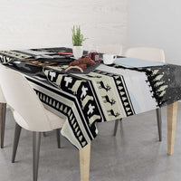 Draped Christmas tablecloth with black-and-white pattern, evergreen trim, and small red accents